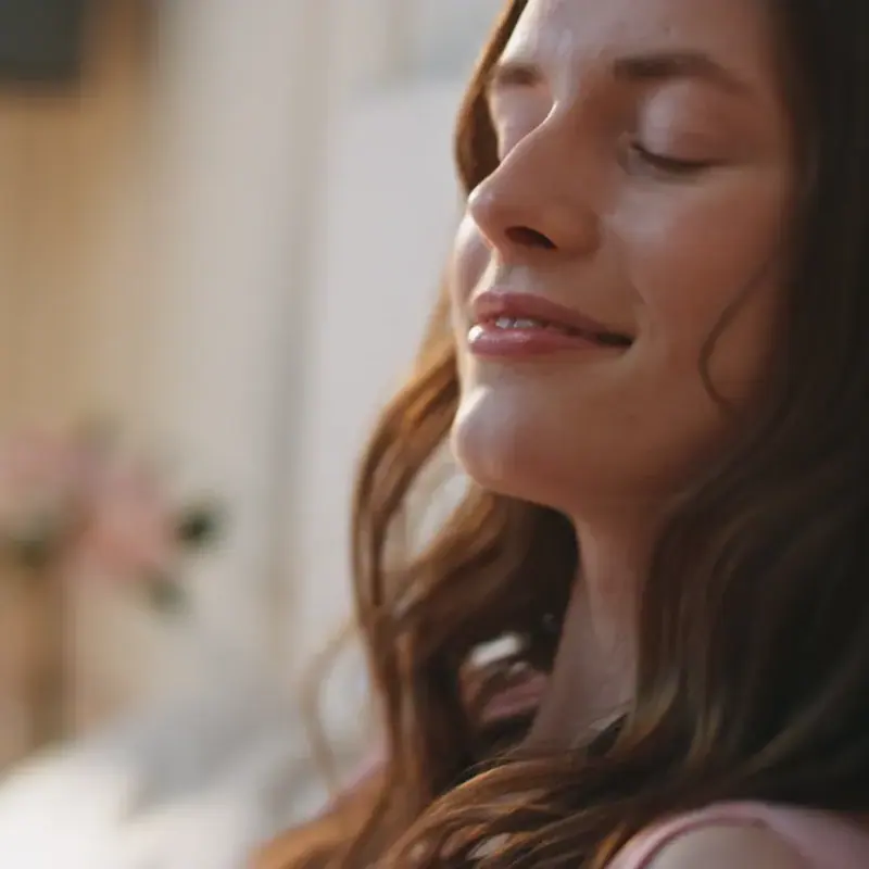 A woman with long brown hair resting with her eyes closed in soft indoor light