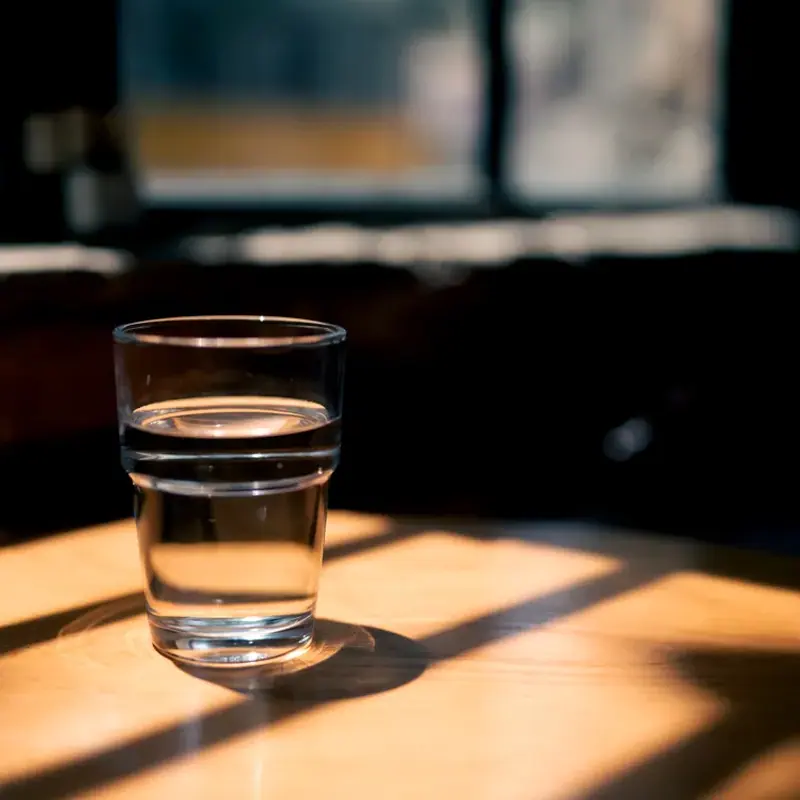 A glass of water on a wooden table in a shaft of warm, low sunlight